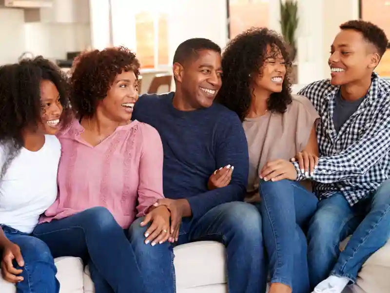 Black family laughing together while sitting on the couch.