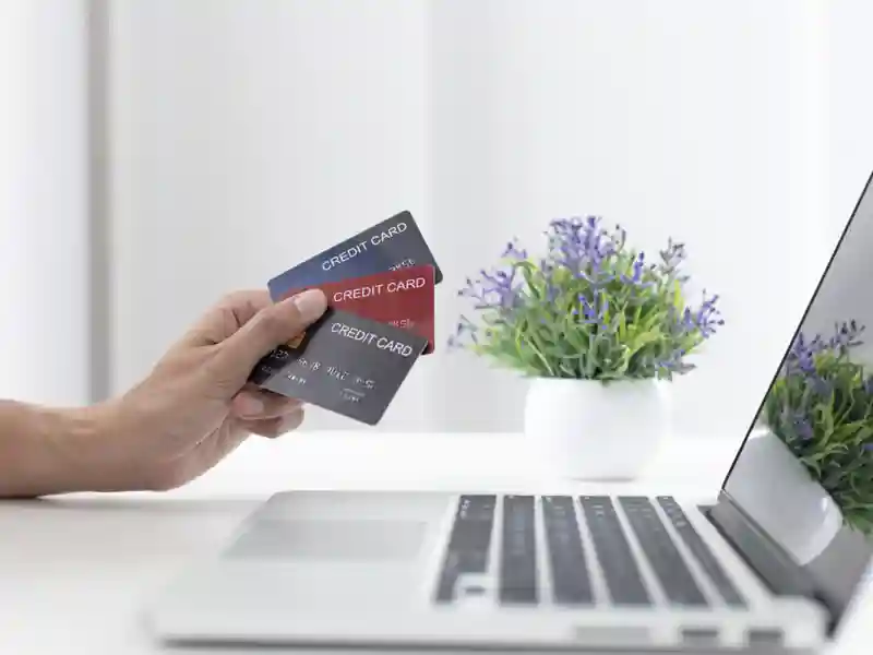 Person holding up three credit cards in front of a laptop.