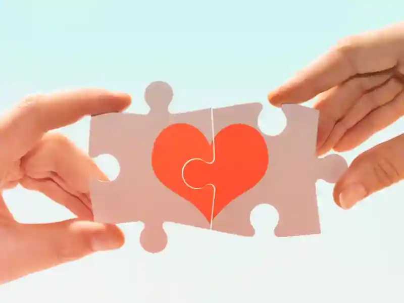 Hands holding up two puzzle pieces showing a heart.