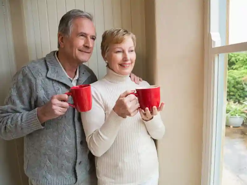 Senior couple holding red mugs at home in the kitchen.