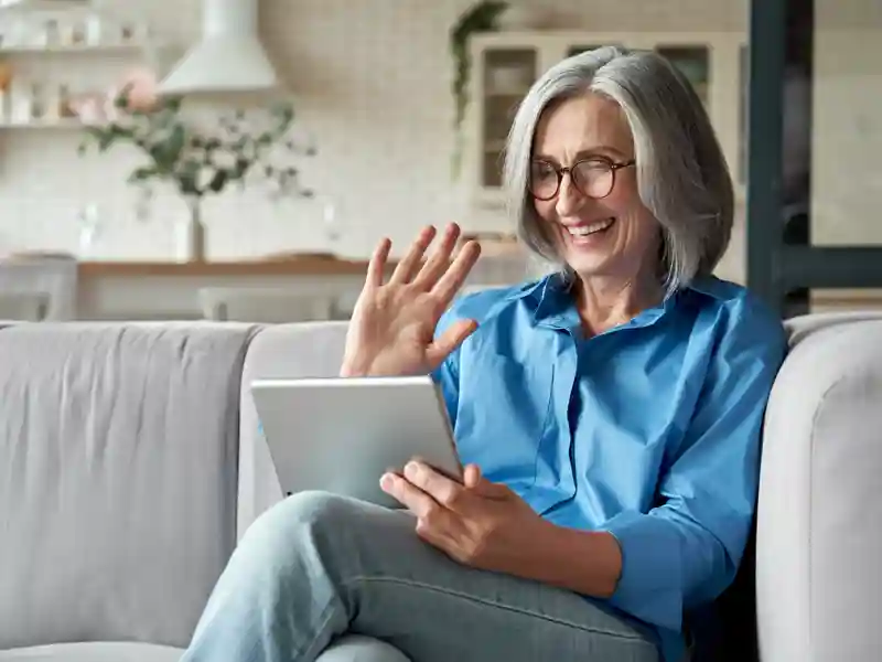 Adult woman waving hand holding digital tablet computer on a video conference